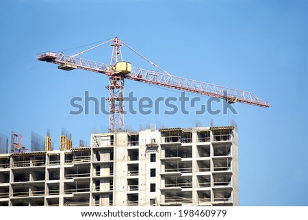 Big hoisting tower crane and top of construction building over cloudless sky