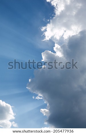 Landscape with sun rays through white clouds on blue sky. Vertical photo