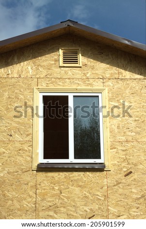 Wall from wooden panels made of pressed sandy brown wood shavings with white plastic window and roof in a new house vertical photo closeup