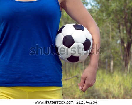 Teenage girl in blue shirt and yellow shorts holding classic ball for playing soccer. Closeup Photo