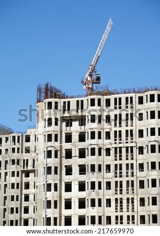 Big hoisting tower crane and top section of modern construction building over cloudless sky