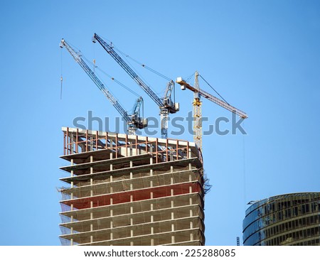 Hoisting tower cranes in construction process on top of office building construction over clear blue sky