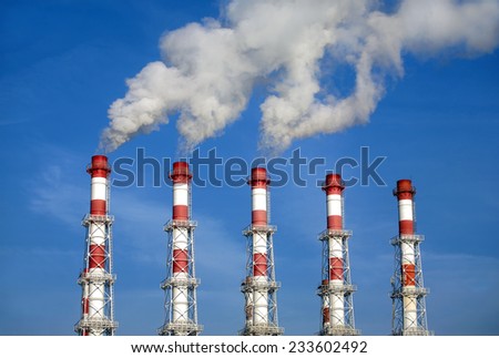 Five red and white industrial pipes with white smoke over blue sky. Horizontal photo