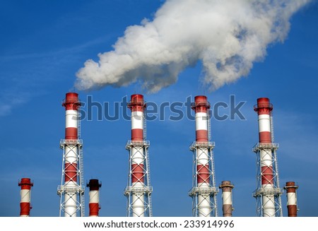 Many red and white industrial pipes with white smoke over blue sky. Horizontal photo