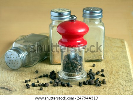 Still life with black peppercorn, hand mills and glass spice jars on kitchen table. Photo closeup