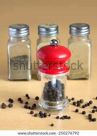 Still life with black peppercorn, hand mills and glass spice jars on wooden surface. Vertical photo closeup