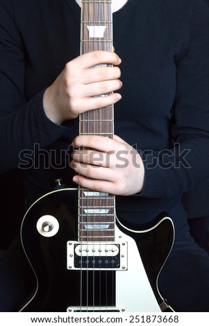 Girl vertical holds black electric guitar neck closeup. Image isolated on black background