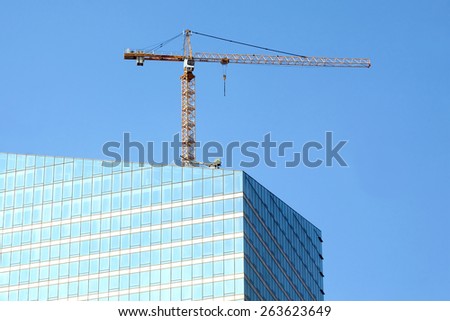 Yellow hoisting tower crane on top of construction skyscraper building over blue sky