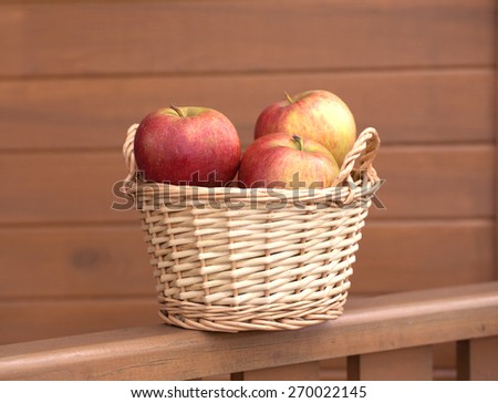 Ripe red and yellow apples in light brown wicker basket on wooden fence closeup