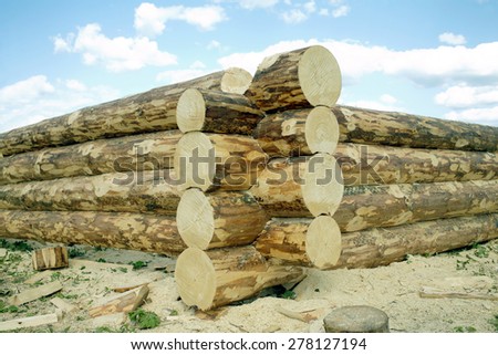 Beginning of rural house construction from heavy logs against blue sky with white clouds in summer day