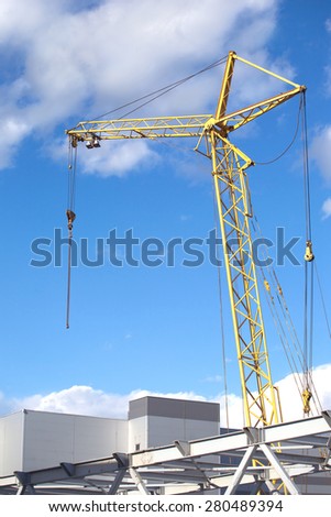 Tower crane on industrial building construction over blue sky with light white clouds vertical view