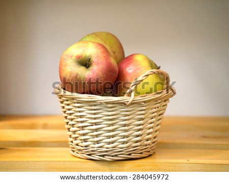 Ripe red and yellow apples in light brown wicker basket on wooden table on a shelf closeup