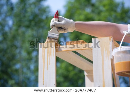 Female hand in textile glove paint wooden furniture outdoors closeup