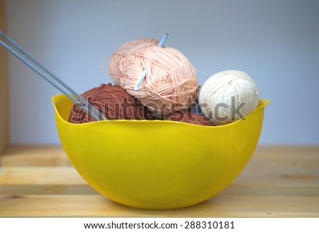 Color skeins of wool yarn, knitting needles and crochet hook in a big yellow bowl on wooden shelf. Photo closeup