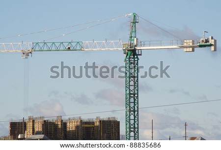 Green and white hoisting crane on building construction