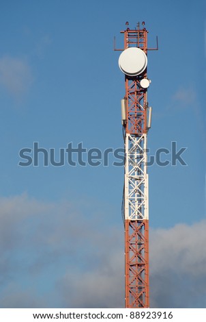 High red and white cellular tower with aerials over sky