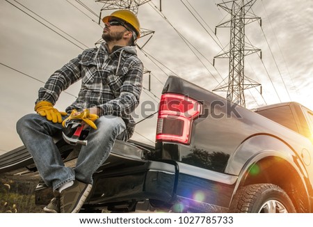 Caucasian Field Worker with Tools. Caucasian Men Wearing Safety Gloves and Hard Hat Seating on the Back of His Pickup Truck. Contractor in the Field