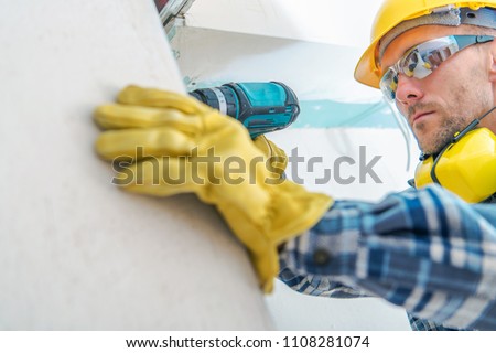 Contractor Remodeling Job. Caucasian Worker with Cordless Driller Installing Drywall Elements. Hard Hat Construction Zone