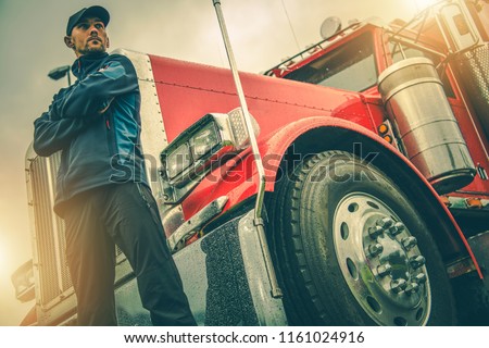 American Trucker Job. Caucasian Truck Driver in Front of His Red Semi Truck.