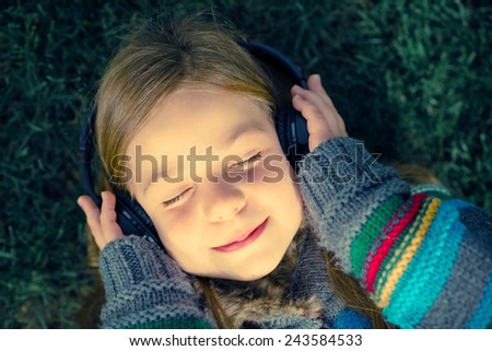 Girl with Wireless Headphones Enjoying Music Laying on Grass in a Park.
