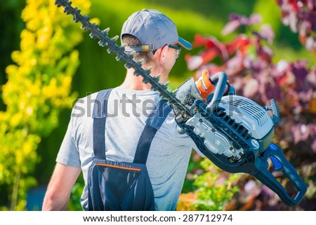 Professional Gardener with Large Gasoline Hedge Trimmer Going to Work. Summer Garden Care.