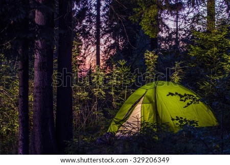 Camping in a Forest. Late Evening on a Camp Site. Green Illuminated Tent Between Spruce Trees. Outdoor Lifestyle.