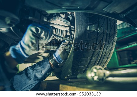 Car Mechanic Fixing Tie Rod and Steering System While Being Under the Vehicle. Car Maintenance in the Professional Service.