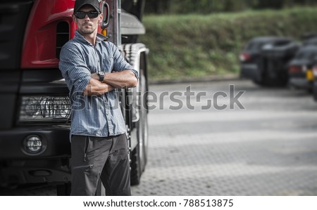 Trucker and His Semi Truck. Caucasian Driver in His 30s in the Delivery Hub. Transportation Theme.