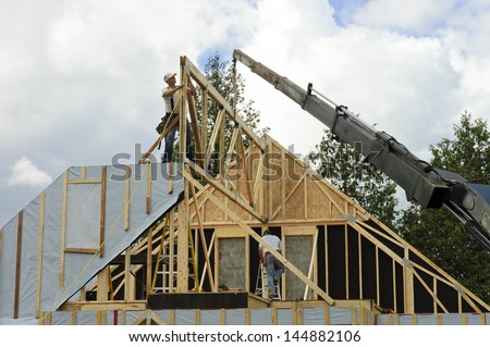 Construction workers framing the roof of a country house with help of a crane in a rural country of Mont-Laurier, Quebec, Canada