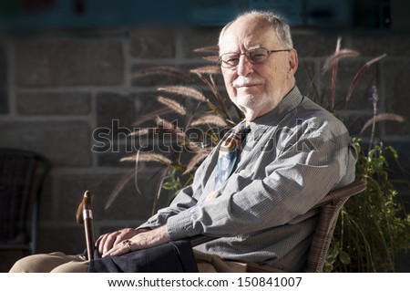 elegant senior gentleman sit on a chair at a wedding ceremony,  holding a walking stick
