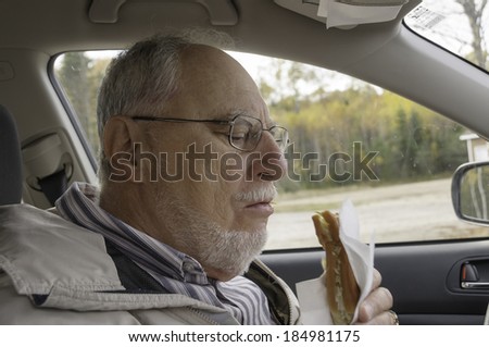 senior man with expressive face eating  fast foods in his car -  french fries and hot dogs