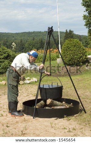 senior preparing camping fire to cook corn in a big iron pot for annual corn party on the beach