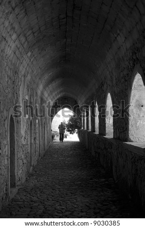 Tourist under the arches alley of the  Greek Orthodox monastery leading to the light entrance, Crete, Greece,\