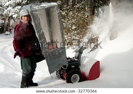 senior in winter suit behind a plastic shelter with snow blower after  storm in Quebec, Canada