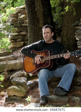 mature man guitarist sit on stone stairs in garden playing guitar