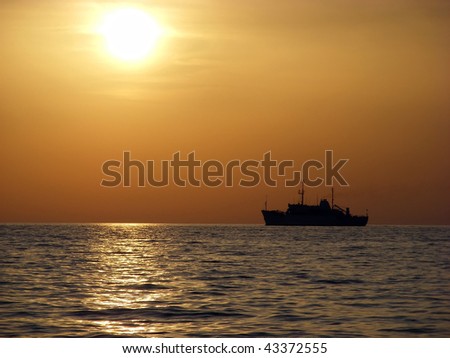 In sunset cargo ship floats on the sea in the sun