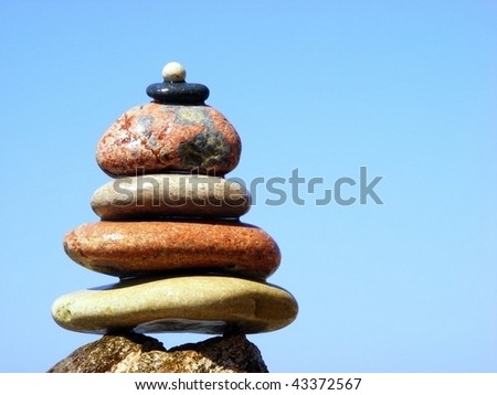The pyramid of stones on a background of sea and sky with the horizon line in the sun clear cloudless day