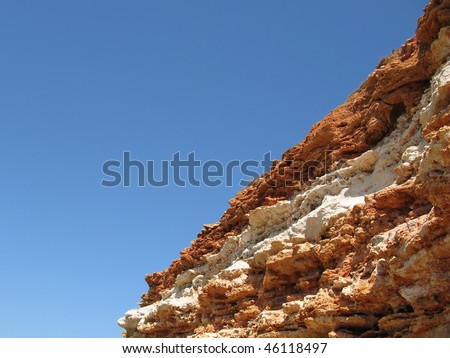 Sheer cliff of layered rocks on the mountain backdrop of blue sky