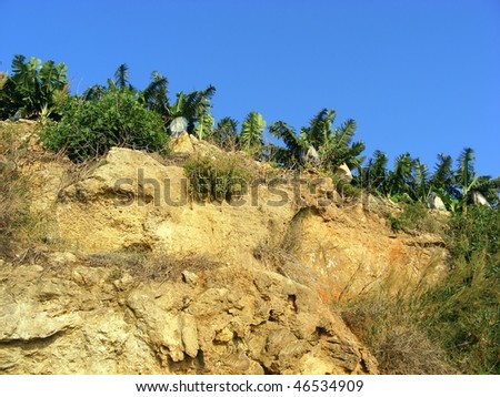 Sheer cliff of layered rocks on the mountain backdrop of blue sky