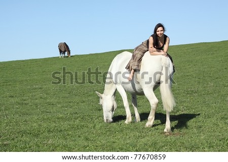 Beautiful young woman and a white horse on green meadow.