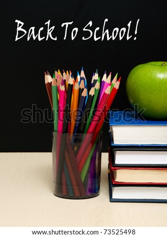 School books with apple on desk, on black school board background