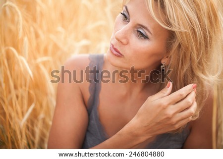 Young woman standing on a wheat field with sunrise on the background