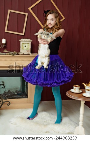 A young girl in the image of Alice in Wonderland stands near the fireplace and holds a rabbit