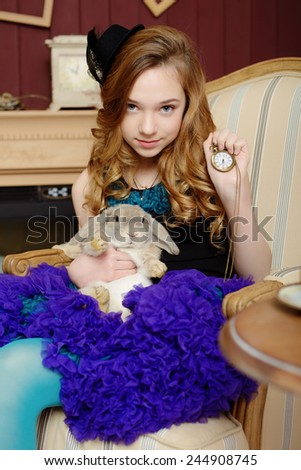 Young girl in the image of Alice in Wonderland is sitting in a chair by the fire, holds a rabbit and a pocket watches
