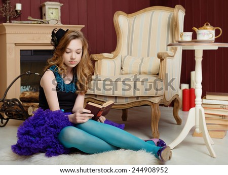 Young girl in the image of Alice in Wonderland is sitting near the fireplace and reading a book