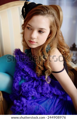 Young girl in the image of Alice in Wonderland is sitting in a chair near the fireplace