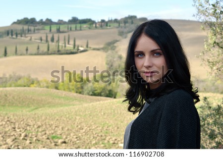 Portrait of a calm young woman with bright blue eyes on idyllic Tuscan landscape background. Italy