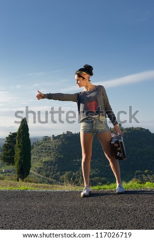 Stylish attractive young woman hitchhiking along a road. Tuscan, Italy