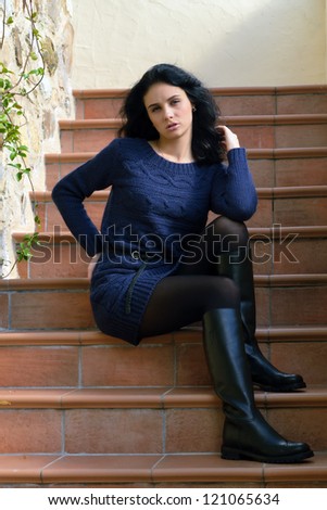 Stylish beautiful girl sits on the stairs near rough stone wall of the old house. Tuscan, Italy