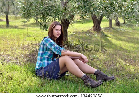 Agritourism. Beautiful young country girl in courtyard sits under olive trees. Tuscan, Italy